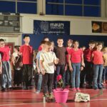 una fila di bambini, uno di loro è qualche passo avanti. vicino a lui c'è un secchio con una rosa rossa