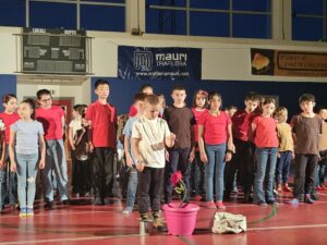 una fila di bambini, uno di loro è qualche passo avanti. vicino a lui c'è un secchio con una rosa rossa