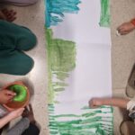 mani di bambini che colorano fogli messi a terra