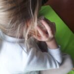 bambina vista di spalle con una conchiglia appoggiata alll'orecchio destro