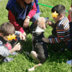 due bambini ed un adulto sono intorno ad un cane che è seduto nel prato