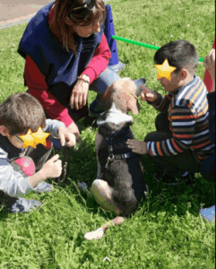 due bambini ed un adulto sono intorno ad un cane che è seduto nel prato