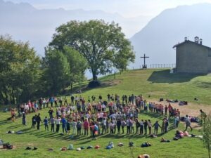 Un cerchio di bambini in un prato, sullo sfondo una chiesetta